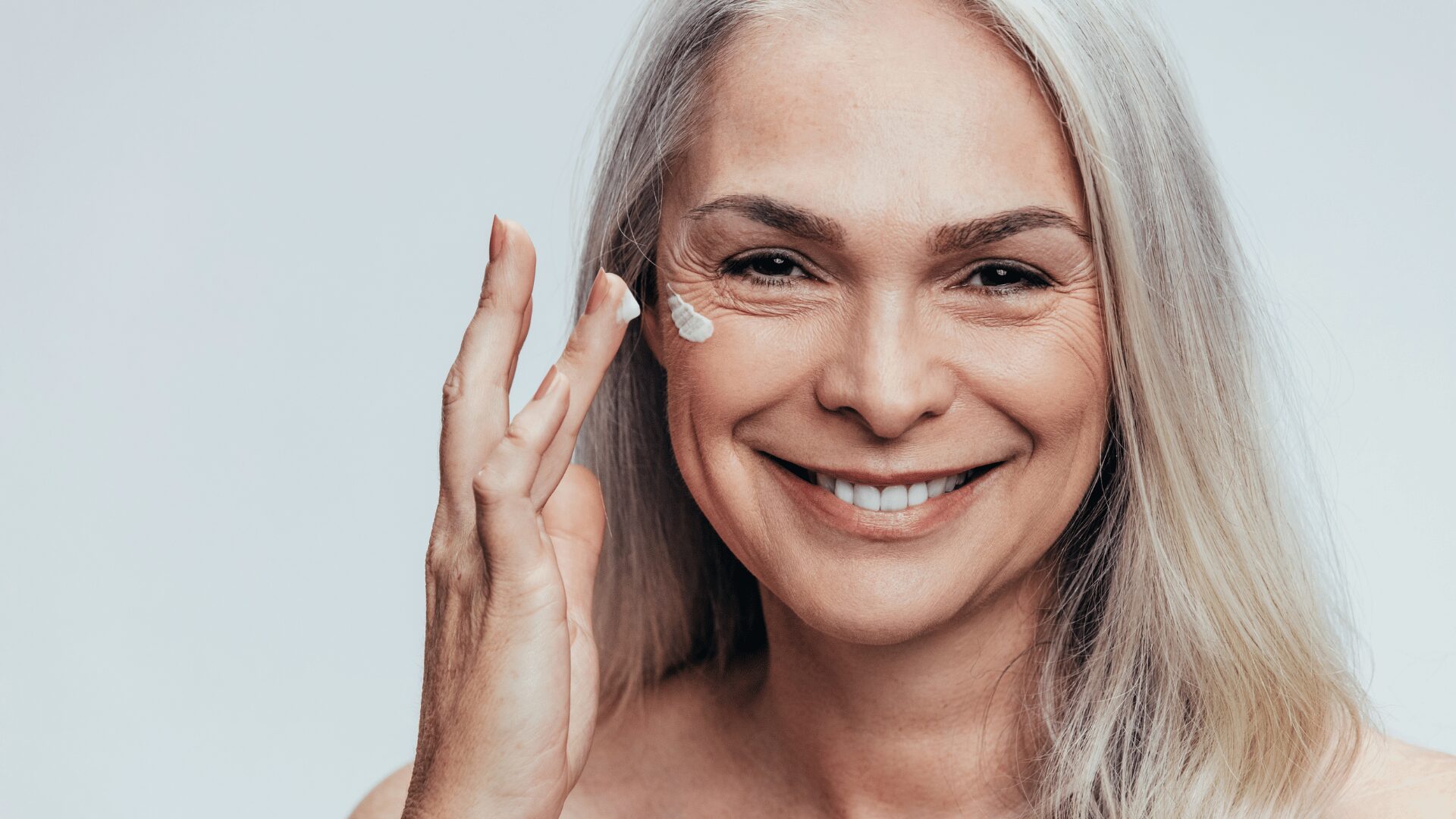 Smiling woman applying anti-wrinkle cream to her face for youthful, glowing skin
